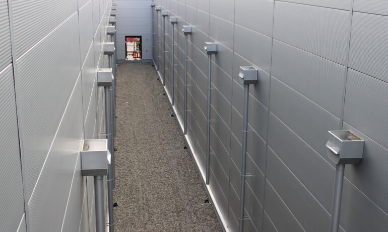 Alleyway with gray metal walls and drainage systems, showcasing Alutech Precision Engineering's innovative design and construction solutions.